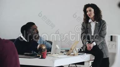 快乐年轻漂亮的高加索商务教练，女人在现代阁楼办公桌上和两个非洲同事交谈。